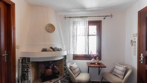 Une pièce chaleureuse avec une cheminée en pierre, deux fauteuils, une petite table et une fenêtre avec un rideau.