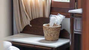 Une chambre avec une tête de lit en bois, une table de chevet, un panier en osier et une fenêtre avec des rideaux.