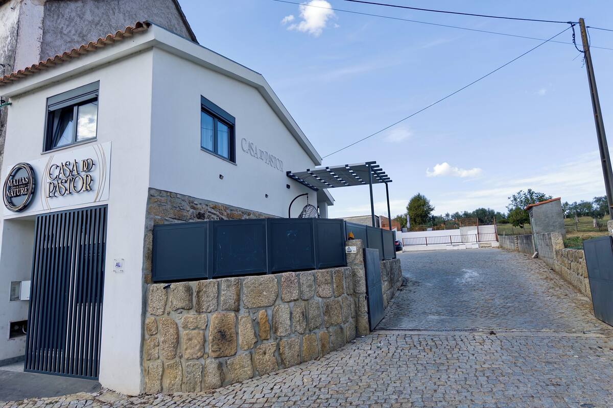 A building with a stone wall and a metal gate, labeled "CASA DO PASTOR".