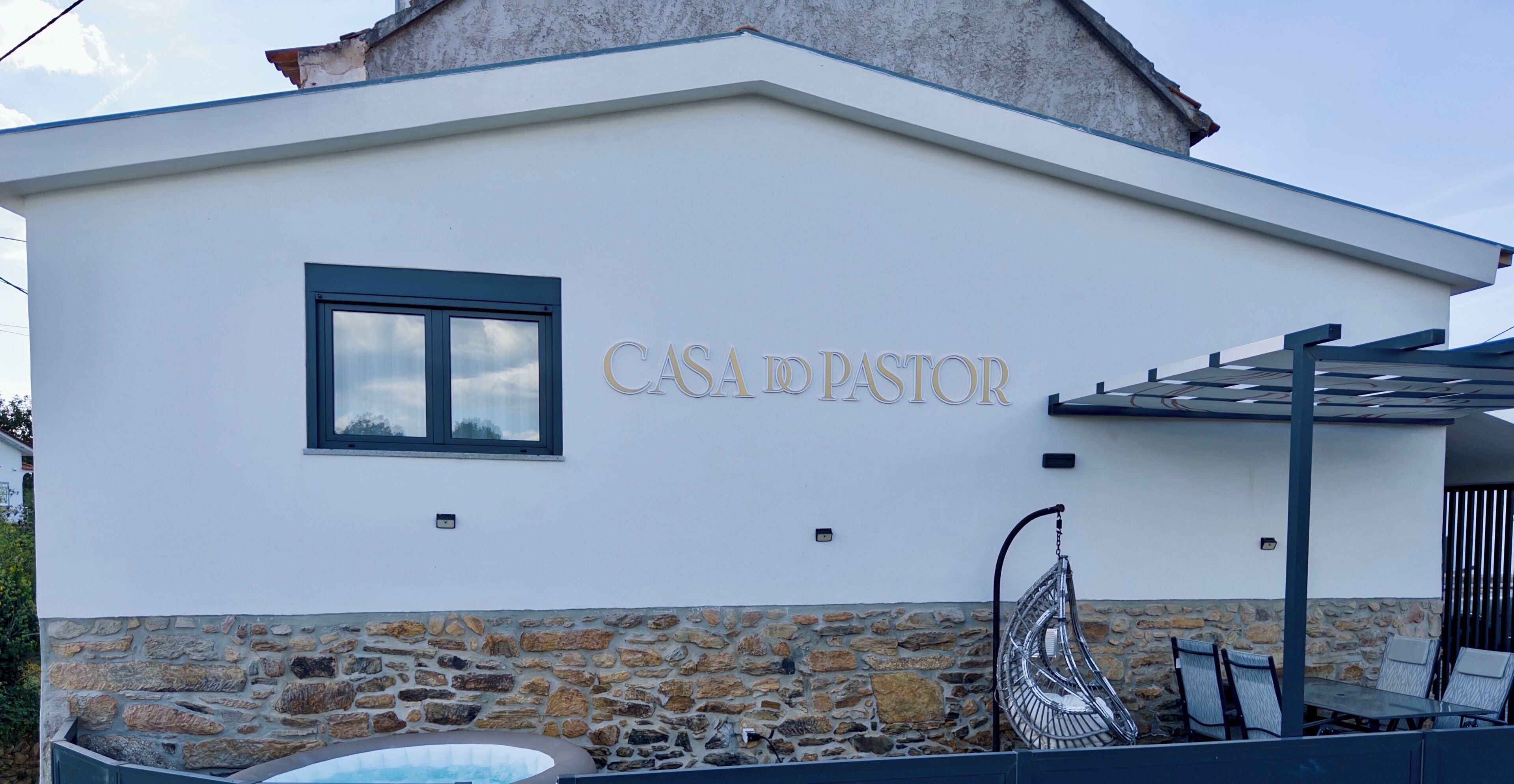 Un edificio con cimientos de piedra y sección superior blanca. Se lee “CASA DO PASTOR” en la pared.