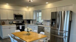Una cocina moderna con armarios blancos, electrodomésticos de acero inoxidable y una mesa de comedor de madera con sillas.
