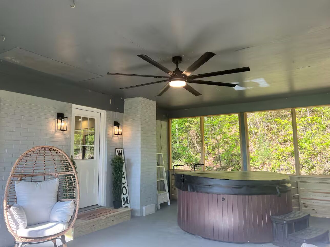 Un espacio al aire libre techado con un jacuzzi, una silla de mimbre y un letrero de bienvenida.