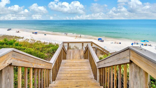 Un escalier en bois menant à une plage, avec un ciel dégagé et une mer calme.