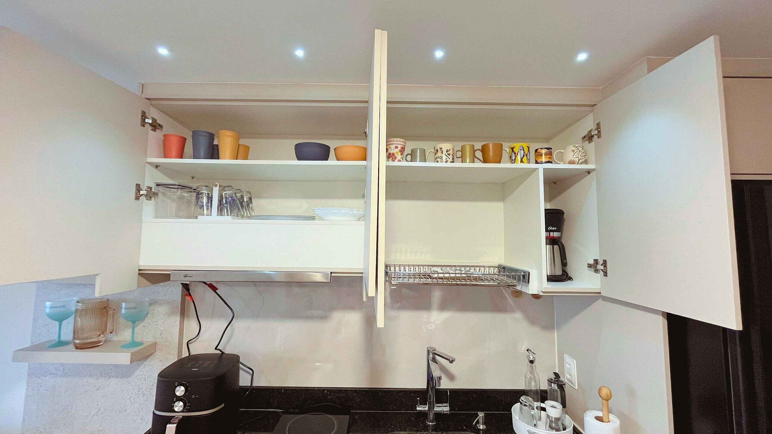 A kitchen with a black countertop, a coffee maker, and a wine glass rack.