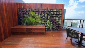 A wooden deck with a built-in planter wall, a bench, and a table with chairs. - Flat Oceânica Seaside - By Almare (João Pessoa)