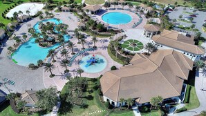 Vista aérea de un complejo turístico con varias piscinas, palmeras y jardines bien cuidados.