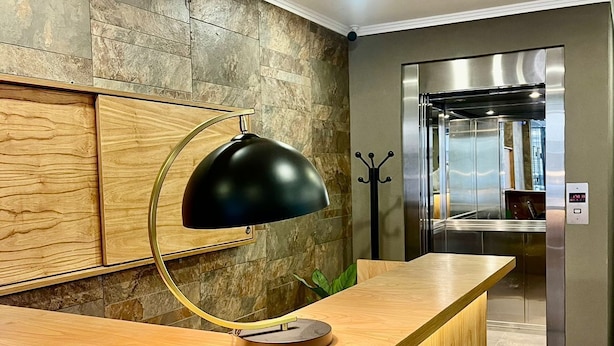 A modern reception desk with a wooden finish, a black pendant lamp, and a stone wall backdrop. - Urbe Hotel (Buenos Aires)