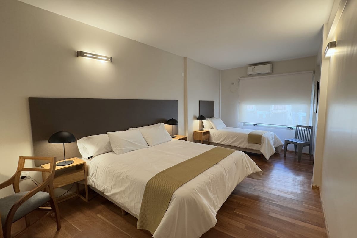 A hotel room with two beds, a desk, a chair, and a window with blinds.
