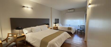 A hotel room with two beds, a desk, a chair, and a window with blinds.
