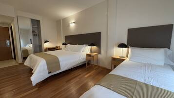 A hotel room with two beds, wooden flooring, and bedside tables with lamps.