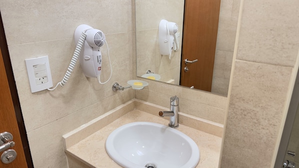 A bathroom with a sink, a hairdryer, a mirror, and a door. - Urbe Hotel (Buenos Aires)