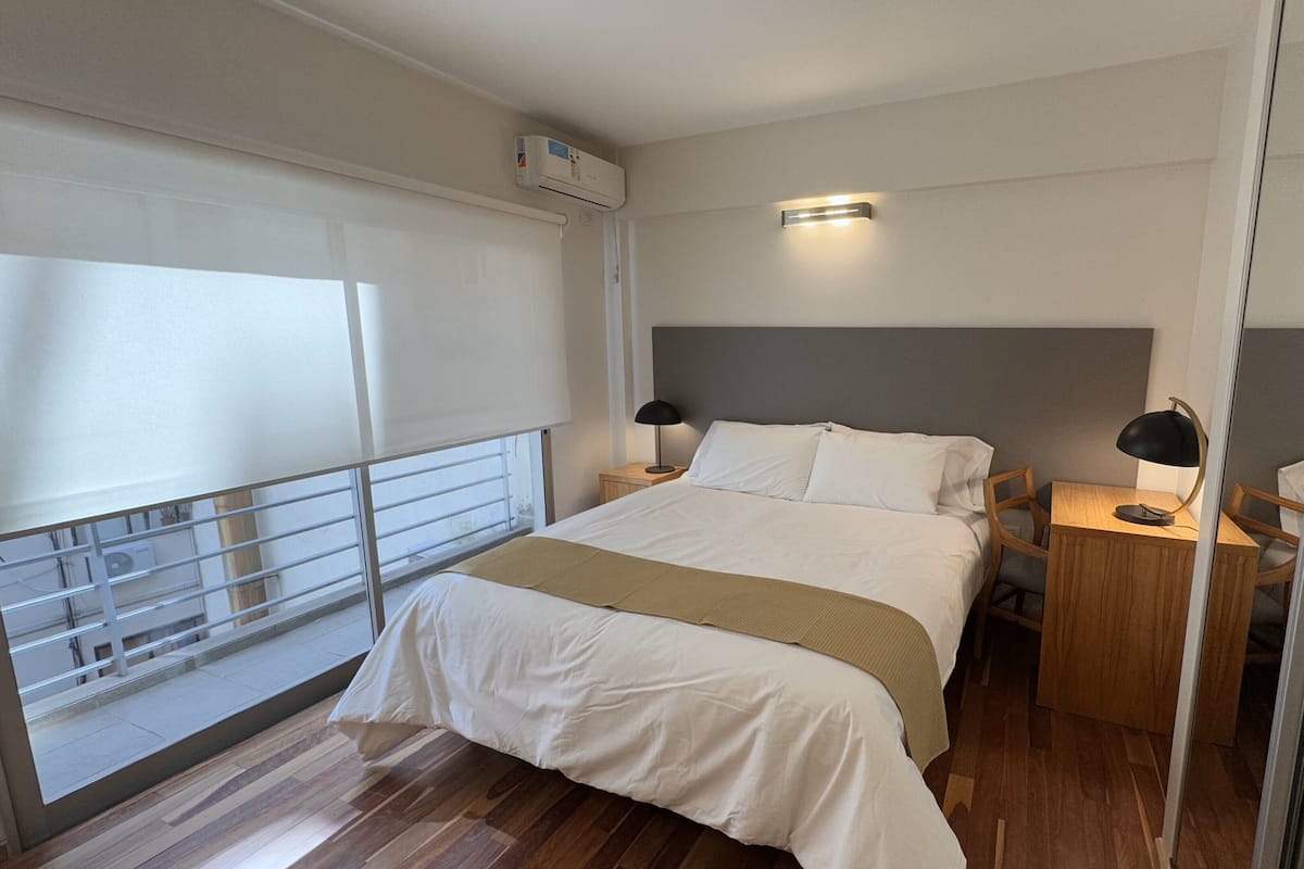 A hotel room with a bed, bedside tables, a mirror, and a balcony with a railing.
