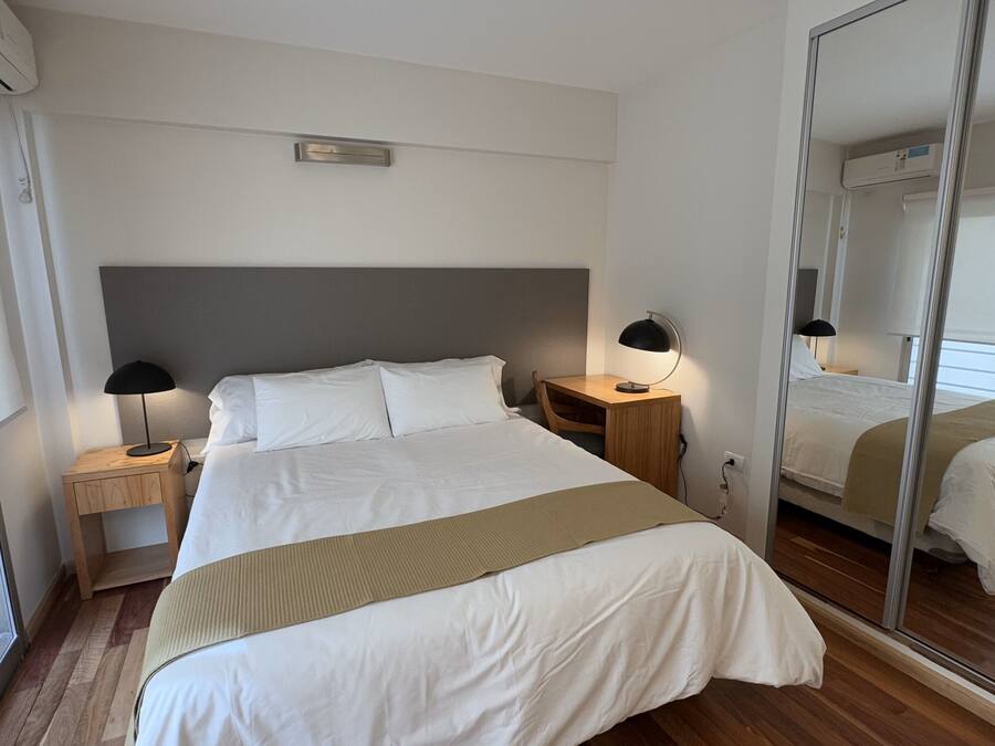 A modern hotel room with a large bed, two bedside tables, a mirror, and a window.