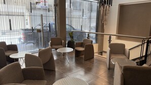 A modern indoor seating area with sofas and round tables, large windows with metal bars, and a staircase with a glass railing. - Urbe Hotel (Buenos Aires)