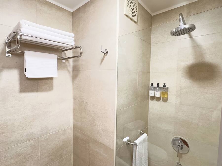 A modern shower with a handheld showerhead, a glass-enclosed shower stall, and a towel rack with folded towels.