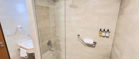 Un baño con ducha envuelta en vidrio, un lavamanos con toalla y artículos de tocador en un estante.