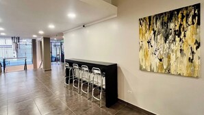A spacious lobby with a reception desk and bar seating, a large abstract painting on the wall, and a view of the outside through a glass door. - Urbe Hotel (Buenos Aires)