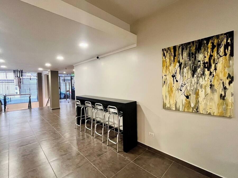 Eine geräumige Lobby mit Empfangsschalter und Bar, ein großes abstraktes Gemälde an der Wand und ein Blick ins Freie durch eine Glastür.