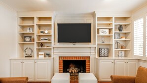 A living room with a fireplace, white shelving units, and a flat-screen TV.
