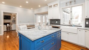 A spacious kitchen with white cabinets, a blue island, and a large window providing natural light.