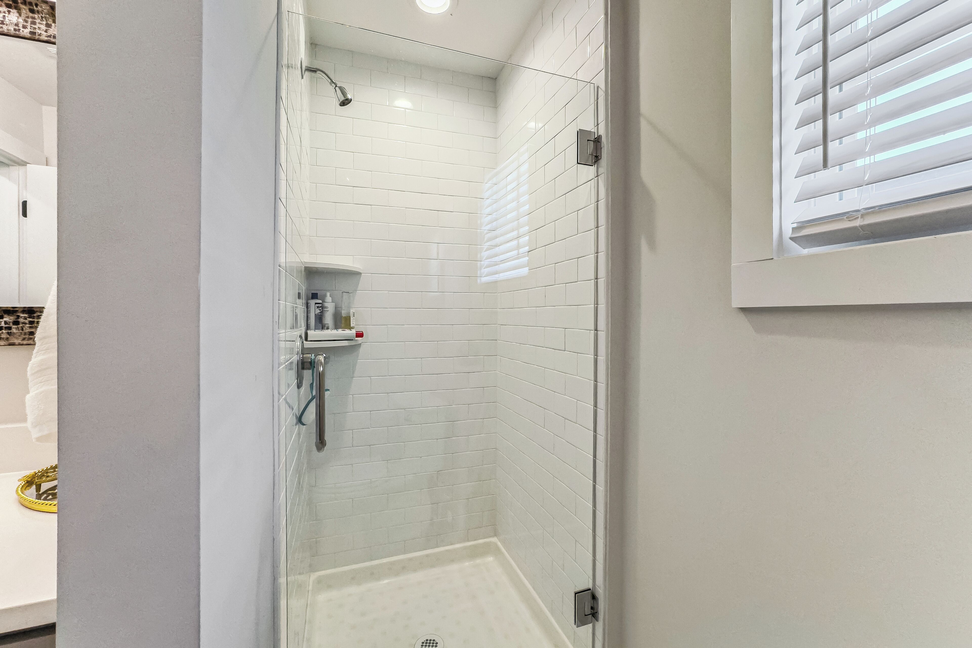 A modern bathroom with white subway tiles, a glass shower enclosure, and a small shelf with toiletries.