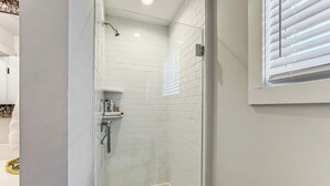 A modern bathroom with white subway tiles, a glass shower enclosure, and a small shelf with toiletries. - Beautiful Historic DT Raleigh (Raleigh)
