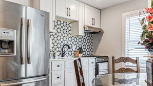 A modern kitchen with a stainless steel refrigerator, white cabinets, a patterned backsplash, and a glass dining table. - Beautiful Historic DT Raleigh (Raleigh)