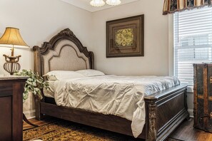 Un dormitorio con una cama de madera, una mesita de noche con lámpara, un cuadro en la pared y una ventana con persianas.