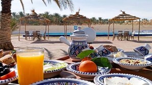 Une table dressée pour le petit-déjeuner sur la plage, avec une nappe, des assiettes, une théière et un verre de jus d’orange.