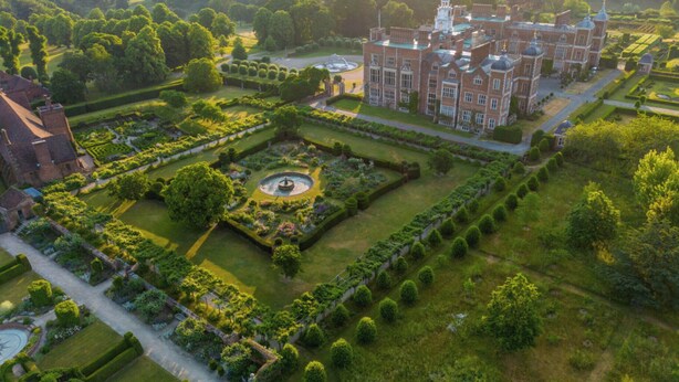 Vista aérea de una extensa y antigua propiedad con un jardín central, jardines formales y un edificio principal con múltiples torres.