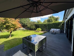 Une terrasse avec une table et des chaises, un grand parasol et un ensemble de meubles de salon.