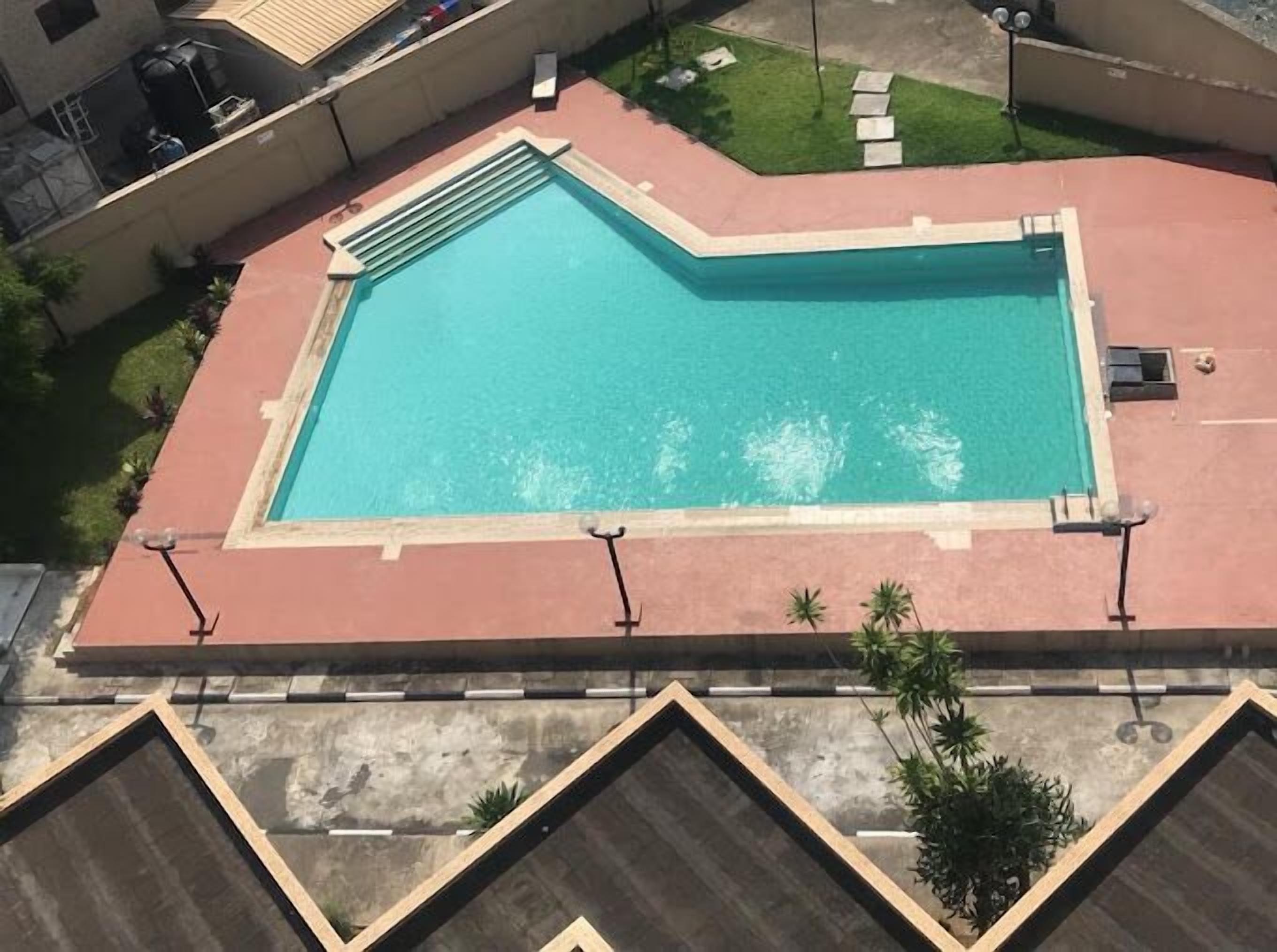 A rectangular swimming pool with a tiled deck, surrounded by a low wall and a small grassy area.