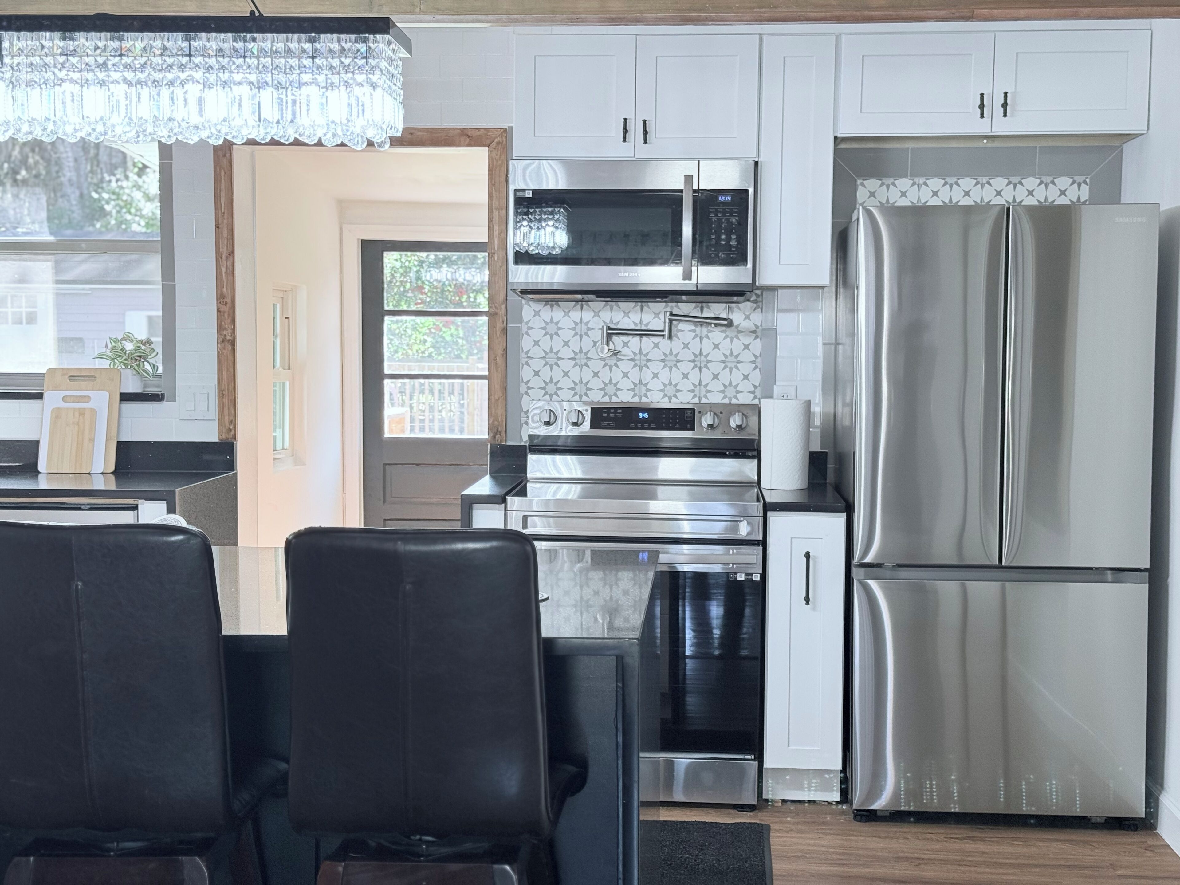 A modern kitchen with stainless steel appliances, a chandelier, and a dining area with black chairs.