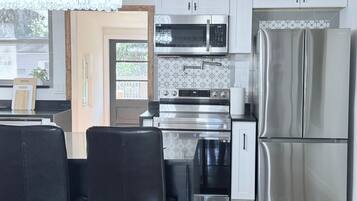 A modern kitchen with stainless steel appliances, a chandelier, and a dining area with black chairs.