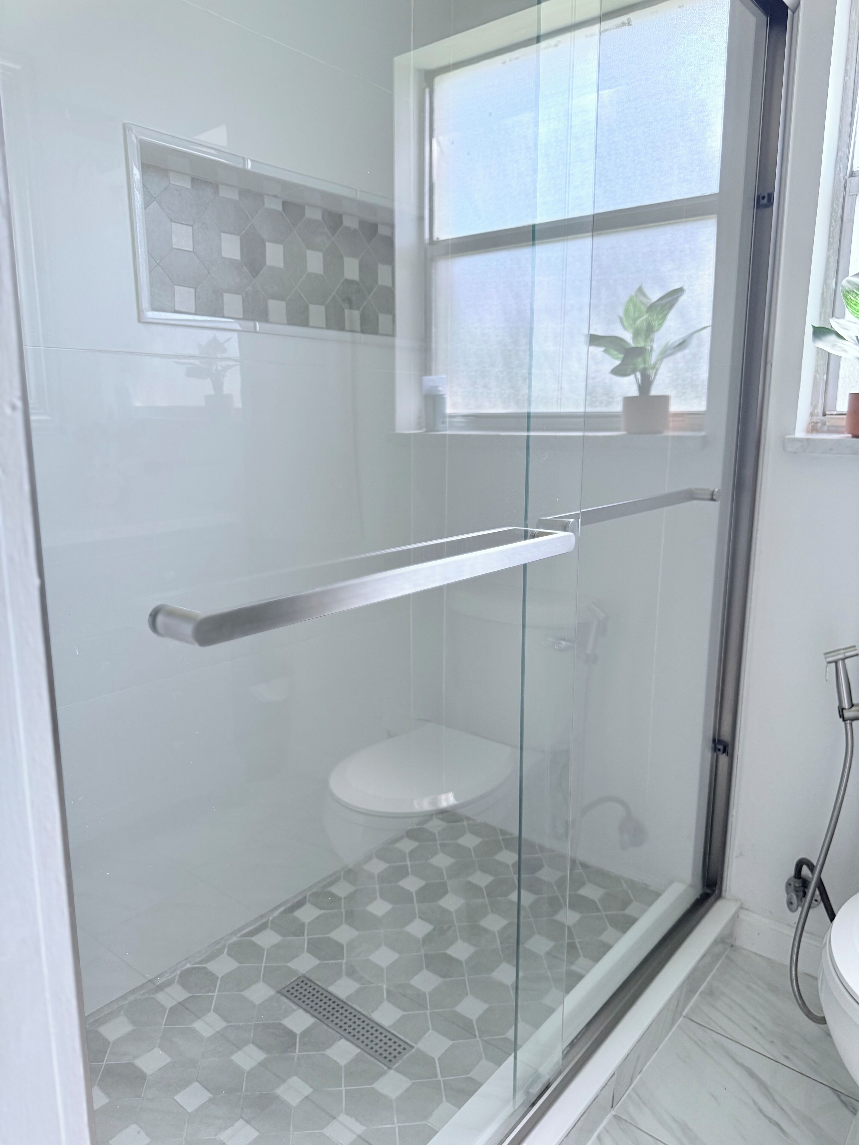 Ein modernes Badezimmer mit einer gläsernen Dusche, einer Toilette und einem Fenster mit einer Pflanze.