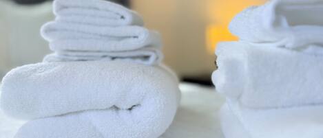 A stack of neatly folded white towels on a textured white surface, likely in a hotel room.