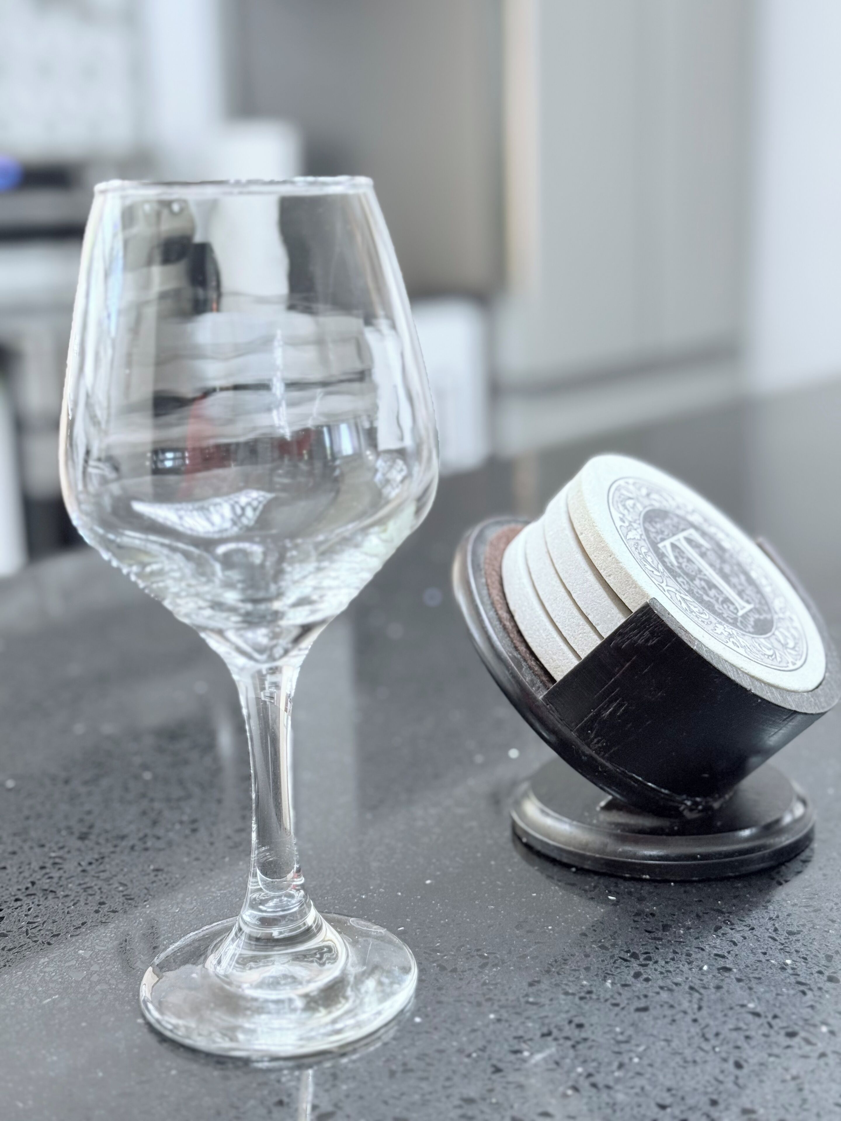 A clear glass wine glass on a dark countertop next to a black and white striped coaster.