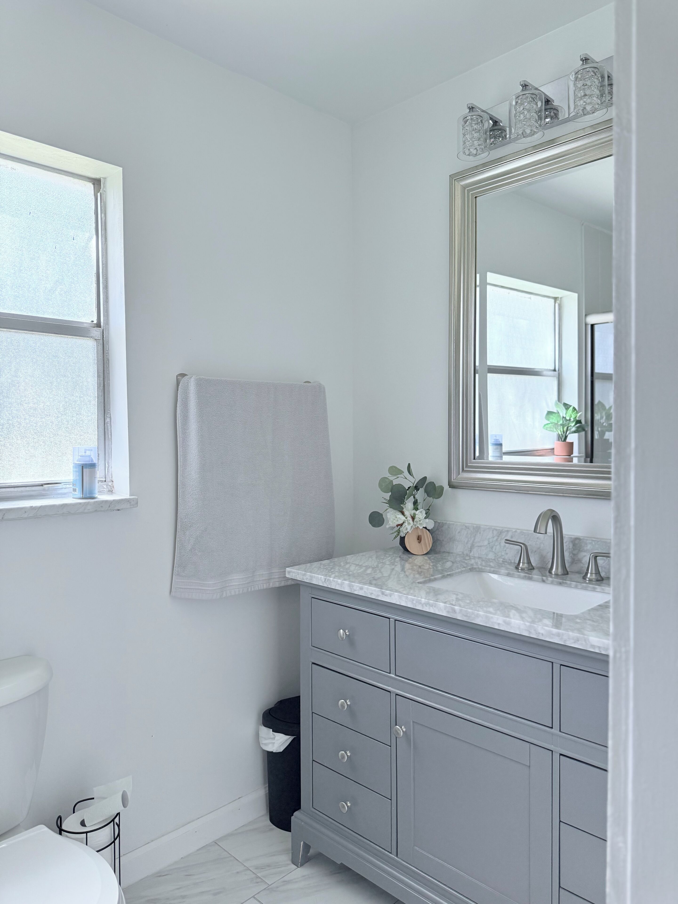 Une salle de bain avec un meuble-lavabo blanc, un grand miroir, une serviette accrochée au mur et une fenêtre donnant sur un beau paysage.