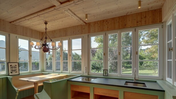 A spacious kitchen with large windows, wooden cabinetry, and a built-in bench. - New top-equipped vacation apartment - 20m to the lake in historic monastery fiefdom (Tegernsee)