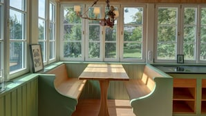 A room with a wooden ceiling, large windows, a central table, and green upholstered seating. - New top-equipped vacation apartment - 20m to the lake in historic monastery fiefdom (Tegernsee)