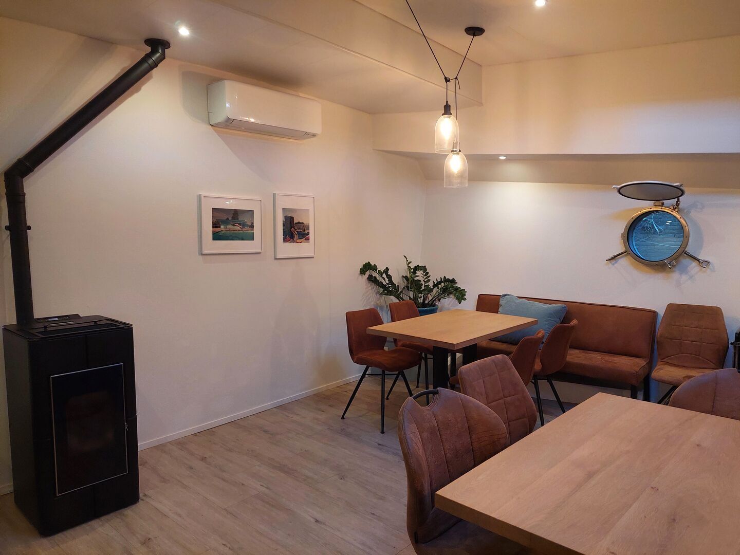 Un'area pranzo moderna con tavolo in legno e sedie in pelle marrone, un termosifone nero e un condizionatore d'aria a parete.
