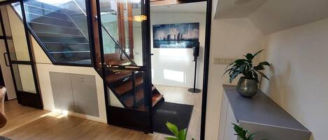 A modern interior with a staircase leading to an upper level, a large window, and a potted plant.