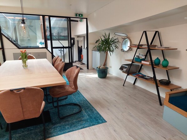 A modern meeting room with a wooden table, leather chairs, a blue rug, a potted plant, and a bookshelf with decorative items.