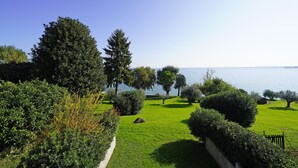 A well-maintained garden with a variety of trees and shrubs, a clear sky, and a view of the water body in the background. - Il Melagrano A12 by Wonderful Italy (Padenghe sul Garda)