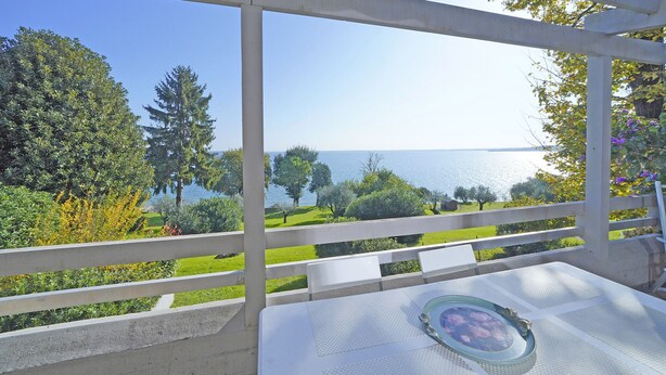 A balcony with a white table and chairs, overlooking a body of water and greenery. - Il Melagrano A12 by Wonderful Italy (Padenghe sul Garda)