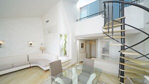 A spacious living area with a glass coffee table, modern furniture, and a spiral staircase. - Il Melagrano A12 by Wonderful Italy (Padenghe sul Garda)