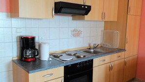 A compact kitchen with wooden cabinets, a black range hood, a coffee maker, a dishwasher, and a sink. - Cozy Retreats in Crikvenica Quiet Neighborhood (Crikvenica)