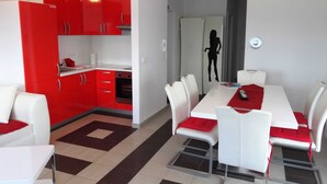 A modern kitchen with red cabinets and a dining area with white chairs and a red table runner.