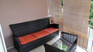 A balcony with a black wicker sofa, a small table, and a green basket.