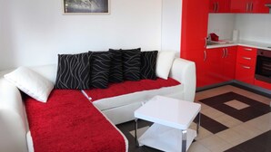 A modern living room with a white sofa, red accents, and a painting of horses.
